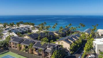 A coastal hotel with multiple buildings, a tennis court, and palm trees.