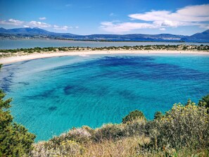 A coastal landscape with clear blue waters, sandy beach, and distant mountains.