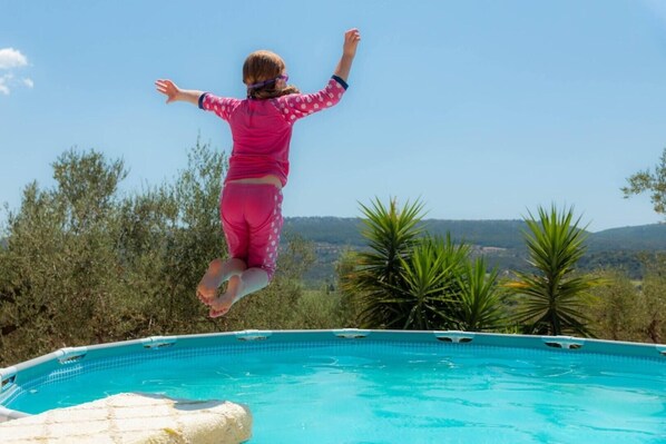 A person jumping into a clear blue pool with a view of trees and hills in the background.