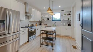Une cuisine moderne dotée d’appareils électroménagers en acier inoxydable, de meubles blancs, d’un îlot central et de luminaires suspendus.