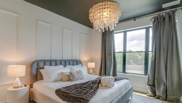 Une chambre moderne avec un grand lit, un lustre et une vue sur l’extérieur.