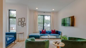 Un salon moderne avec un canapé bleu, des fauteuils verts, une table basse et de grandes fenêtres.