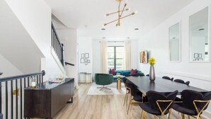 Un espace repas moderne avec une longue table, des chaises sombres et un escalier sur le côté gauche.