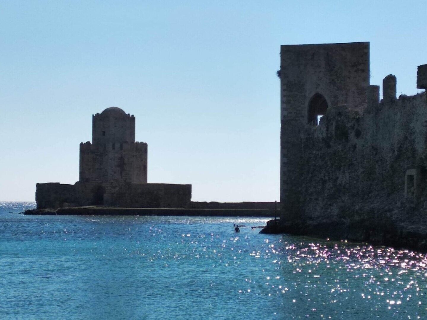 A historical stone structure by the sea, featuring a prominent tower and an arched window.