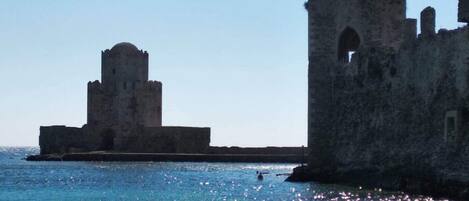 A historical stone structure by the sea, featuring a prominent tower and an arched window.