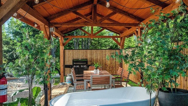 A covered outdoor area with a barbecue grill, a table with chairs, and a large bathtub. - Traverse City - Luxury on the Edge -13 (Williamsburg)