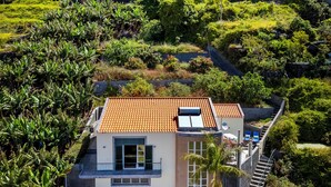 A hillside house with a tiled roof, a green door, and a small outdoor seating area with chairs. - A peaceful, relaxing place with privileged view of the sea. (Tabua)