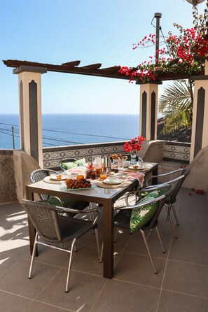 A table set for breakfast with a view of the sea, outdoor chairs, and a pergola with flowers. - A peaceful, relaxing place with privileged view of the sea. (Tabua)