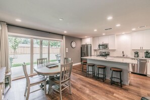 Une cuisine moderne avec des meubles blancs, des appareils en acier inoxydable et un coin bar équipé de tabourets.