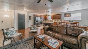 A spacious living room with a leather sofa, a coffee table, and a dining area with wooden chairs and a table. - 15-min Walk to Stadium w/ Huge Yard + Firepit (Arlington)