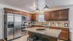 A modern kitchen with wooden cabinets, stainless steel appliances, a granite countertop, and two bar stools. - 15-min Walk to Stadium w/ Huge Yard + Firepit (Arlington)