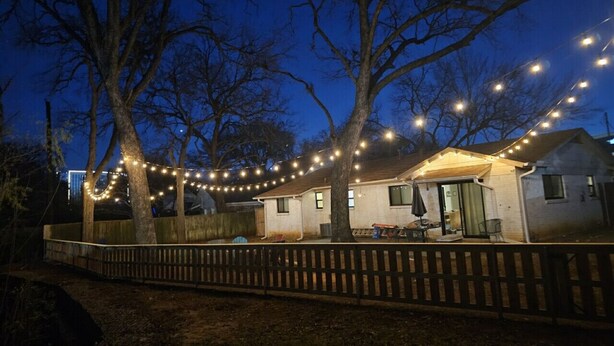 A house with a covered patio, string lights, and a wooden fence. - 15-min Walk to Stadium w/ Huge Yard + Firepit (Arlington)