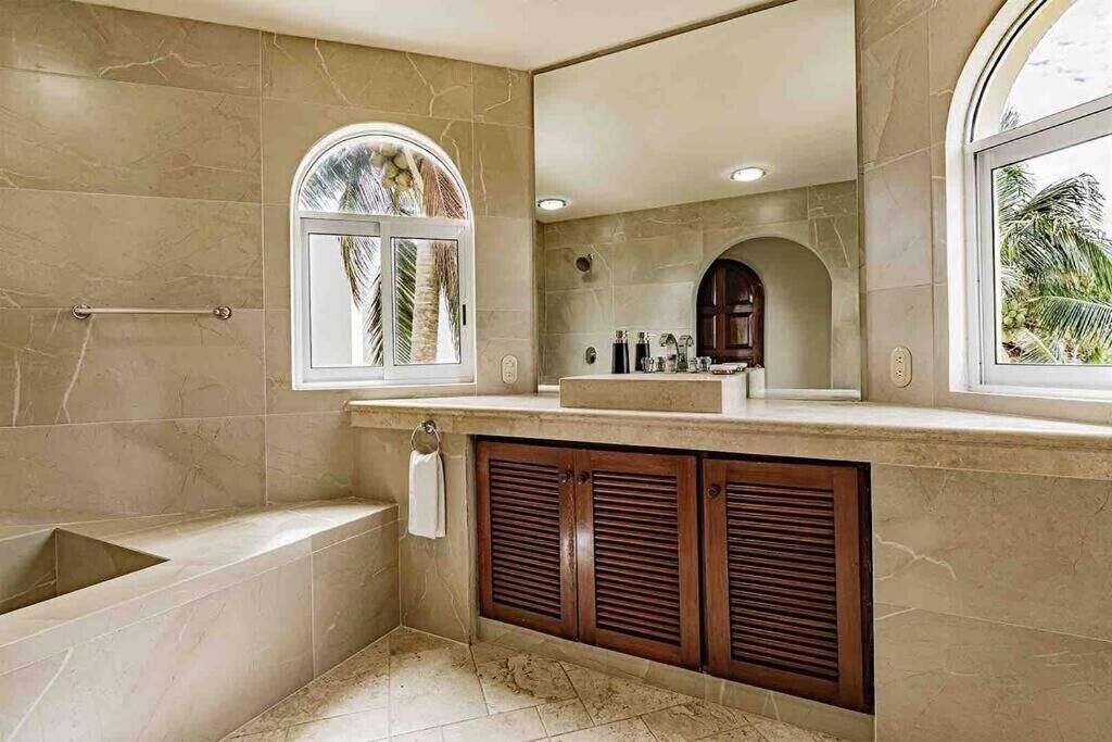 A bathroom with a bathtub, a vanity with a mirror, and a window with a view of palm trees.