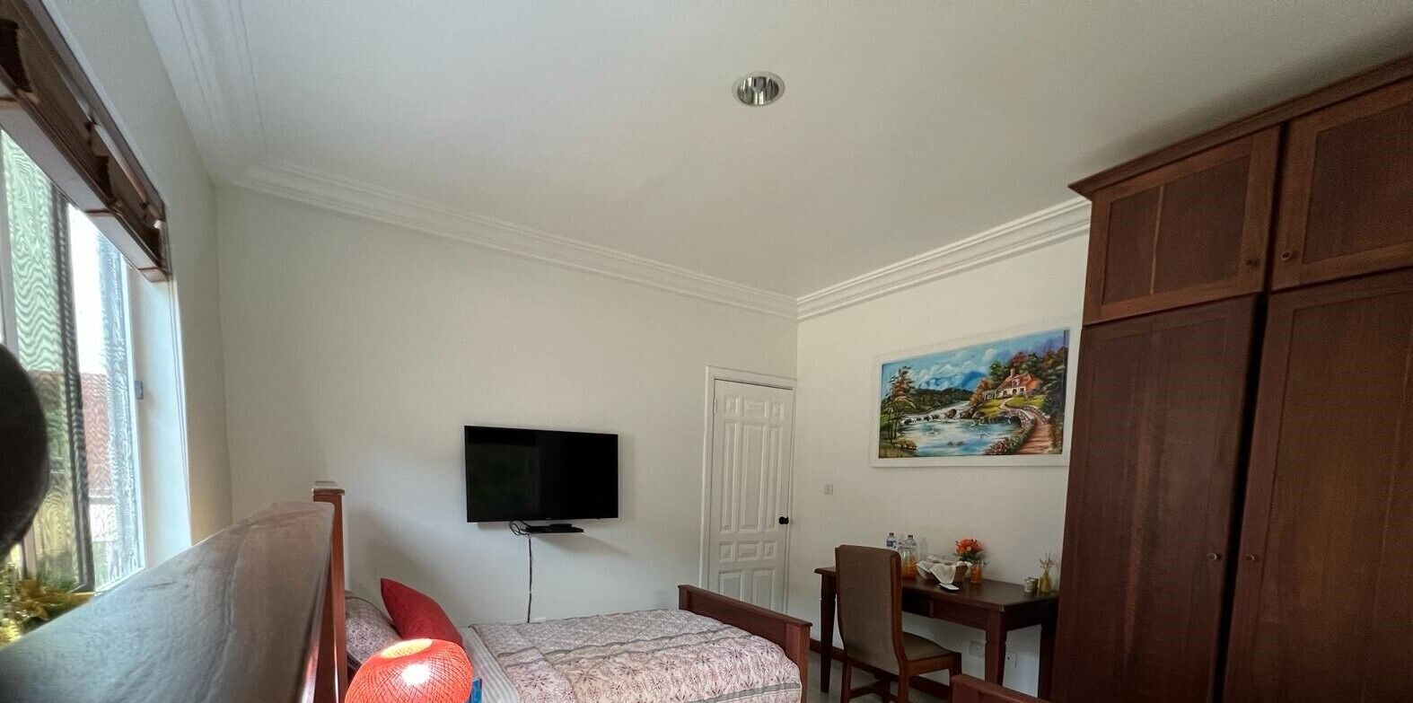 A bedroom with a bed, a desk, a chair, a television, and a painting on the wall.