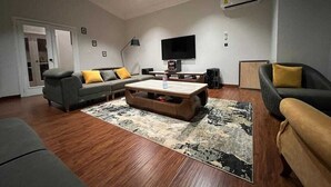 Un salon moderne avec un canapé gris, une table basse en bois et un téléviseur noir fixé au mur.