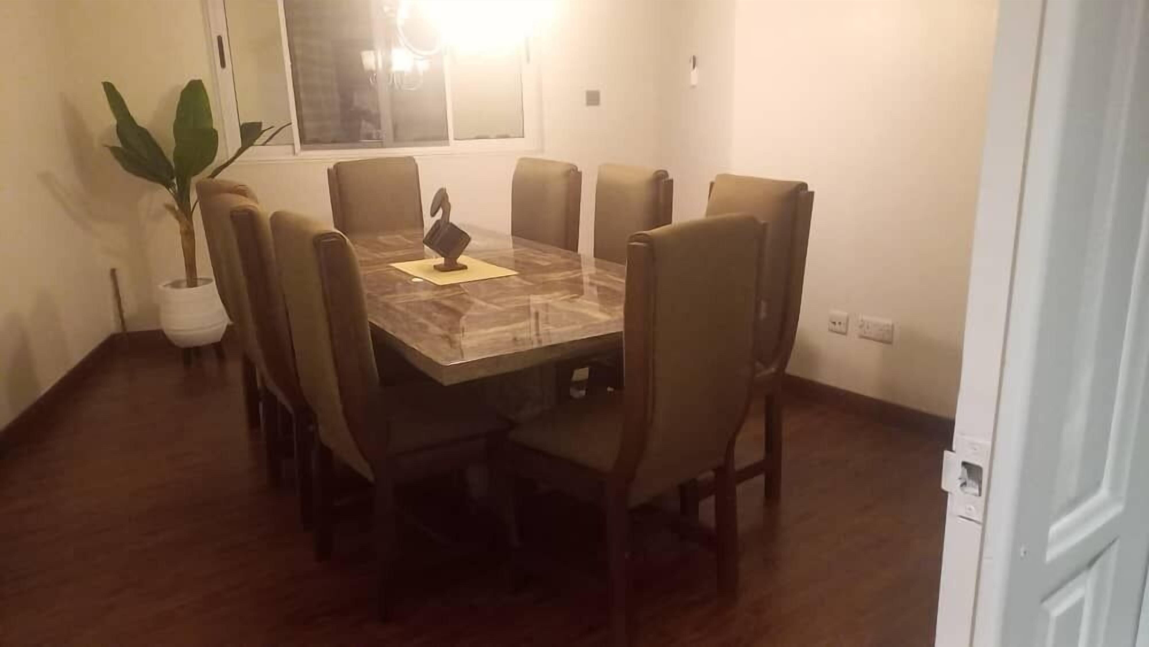 A dining area with a marble table and six chairs, a potted plant, and a window with blinds.