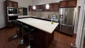 Une cuisine moderne avec des meubles en bois foncé, des appareils électroménagers en acier inoxydable et un îlot central doté de tabourets de bar.