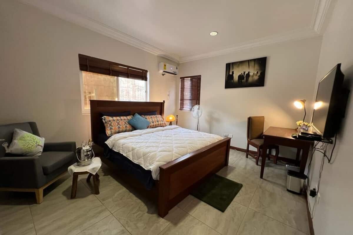 A bedroom with a bed, a chair, a desk, a TV, and a window with blinds.