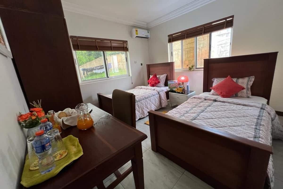 A hotel room with two beds, a small table with breakfast items, and a window with a view of greenery.
