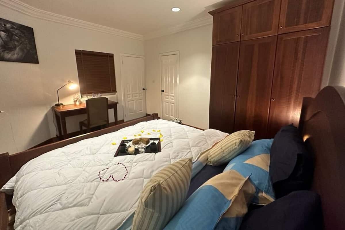 A bedroom with a large bed, wooden wardrobe, and a desk with a lamp.