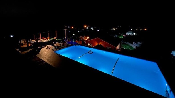 Une piscine illuminée la nuit, entourée de bâtiments et bordée d’un quai.
