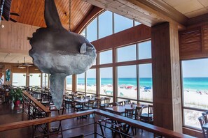 A restaurant with a large fish sculpture hanging from the ceiling, large windows overlooking a beach, and wooden interior design. - Waterfront Villa~Beach~Pool-King Beds (Destin)