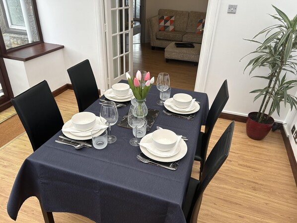 A dining table set with white plates, glasses, and cutlery, a vase with flowers, and a potted plant. - House in Stoneywood,dyce (Aberdeen)