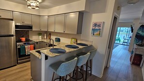 Una cocina moderna con electrodomésticos de acero inoxidable, encimera de granito y taburetes de bar.