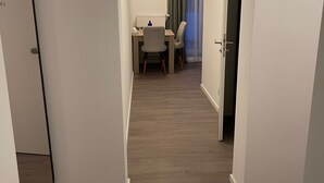 Un corridoio con pavimento in legno, un'area pranzo con tavolo e sedie, e una porta che conduce in un'altra stanza.