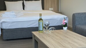 Un letto rifatto con lenzuola bianche, una bottiglia di vino e due bicchieri su un tavolo di legno.