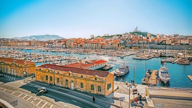 A coastal cityscape with a marina filled with boats, historic buildings, and a prominent hill in the background. - T1 Vieux Port Opera (Marseille)