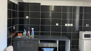 A modern kitchen with black tiled walls, a built-in oven, and a microwave. - T1 Vieux Port Opera (Marseille)