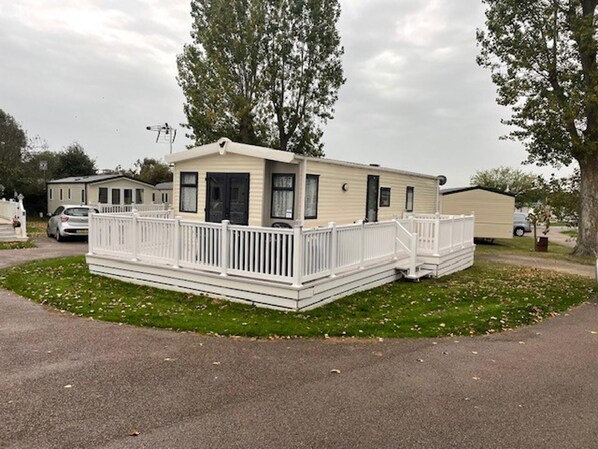A mobile home with a front porch and a fenced deck area. - Premium 2 bed Caravan Sleeps 6 With Huge Decking (Clacton-on-Sea)