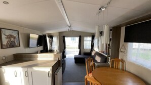 A compact living space with a kitchenette, a dining area, and a seating area with a view. - Premium 2 bed Caravan Sleeps 6 With Huge Decking (Clacton-on-Sea)