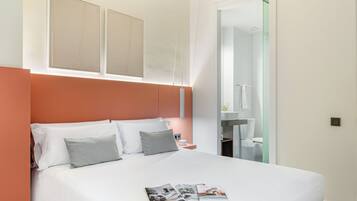 Een moderne slaapkamer met een groot bed, een nachtkastje, een tijdschrift, en een zichtbare badkamer door een open deur.