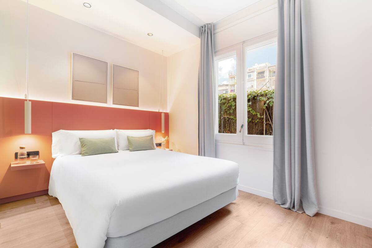 A modern hotel room with a large bed, a nightstand, and a window with curtains.