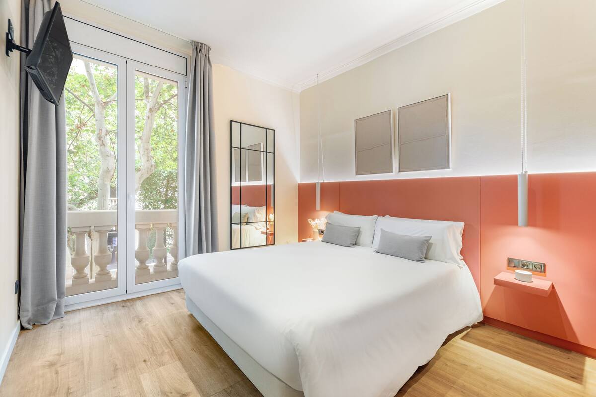 A bedroom with a large bed, a sliding glass door to a balcony, and a wall-mounted TV.