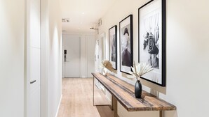 A hallway with a wooden bench, framed pictures on the wall, and a white door at the end. - LeMar by Aspasios (Barcelona)