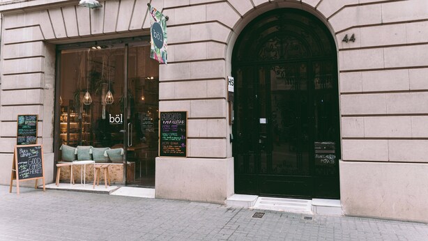 A building with a large arched entrance, a signboard with a menu, and seating outside. - LeMar by Aspasios (Barcelona)