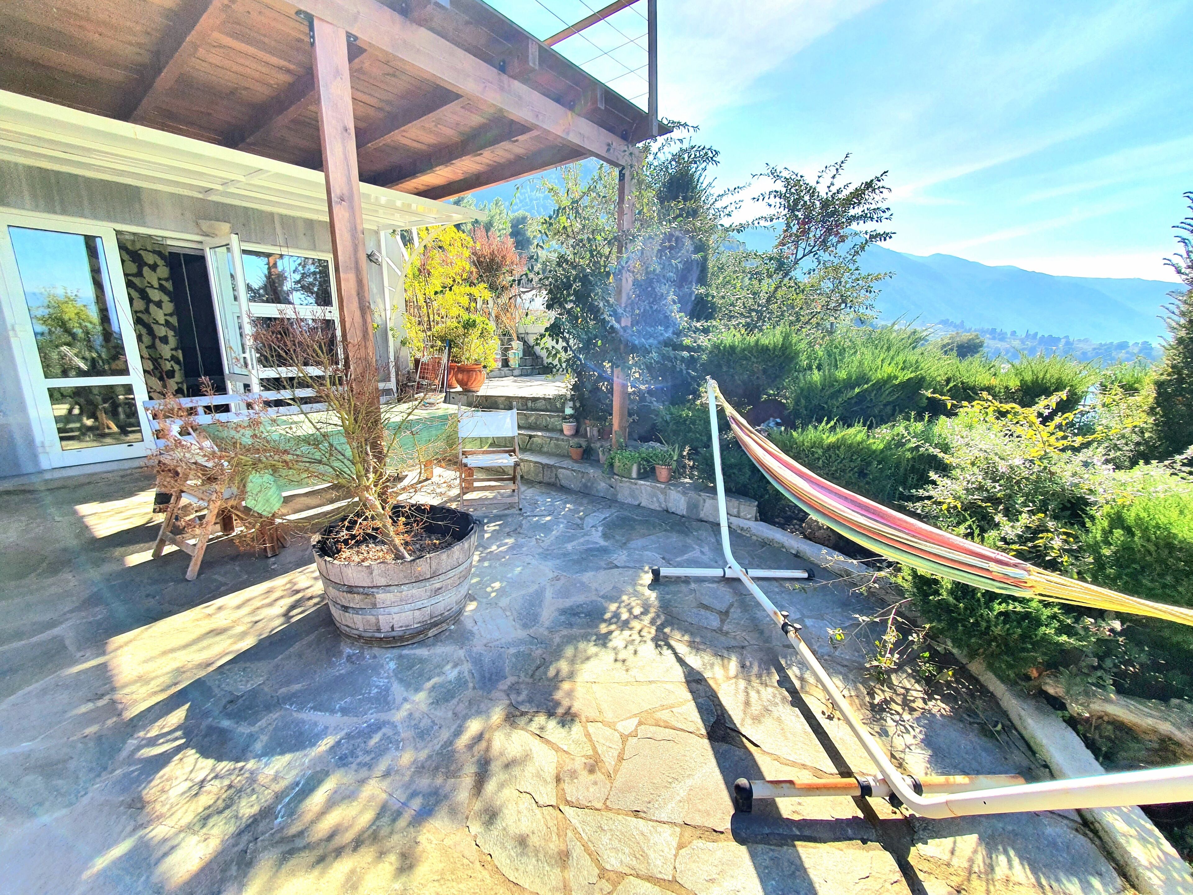 Une terrasse en pierre avec un hamac, des plantes en pot et une chaise.