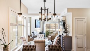 A spacious living room with a large window, a chandelier, and a fireplace.