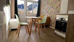 A modern kitchen with wooden flooring, a dining table with chairs, a sofa, and a colorful wall.