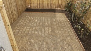 A wooden deck with a gravel surface, surrounded by a wooden fence and a garden area with plants.
