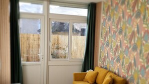 A living room with a sofa, two chairs, a round table, and a window with a view of a fence.