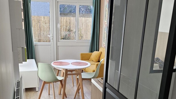A compact living space with a kitchenette, a dining area with a round table and chairs, and a view through a large window.