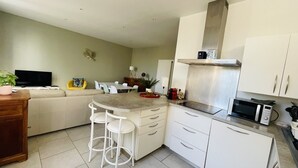Una cocina compacta con armarios blancos, una campana extractora de acero inoxidable, un microondas y una pequeña zona de comedor con una mesa y sillas.