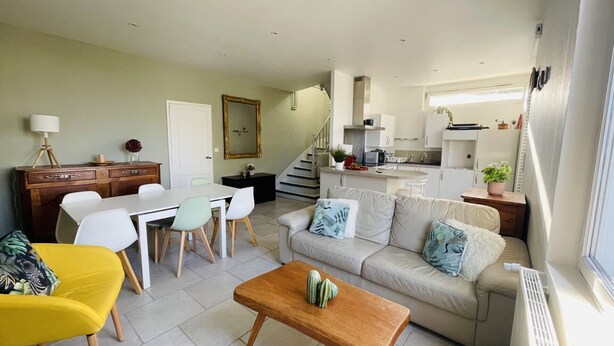 Un espacio habitable compacto con zona de comedor, sofá, mesa de centro y área de cocina con una escalera.