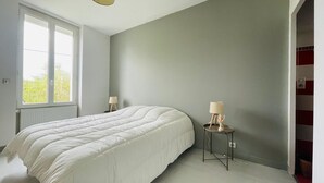Un dormitorio con una cama grande, una ventana y una mesita de noche con lámpara.