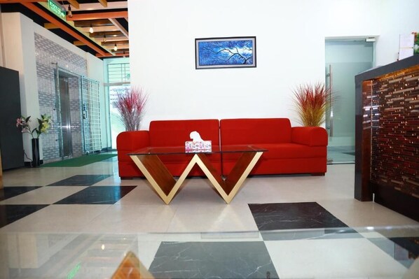 A modern lobby with a red sofa, a glass coffee table, and a framed artwork on the wall. - Grand Castle Hotel (Comilla)