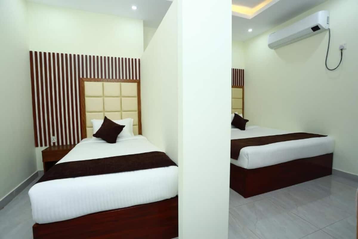 Habitación de hotel con dos camas, un cabecero de madera, una pared blanca y un equipo de aire acondicionado.